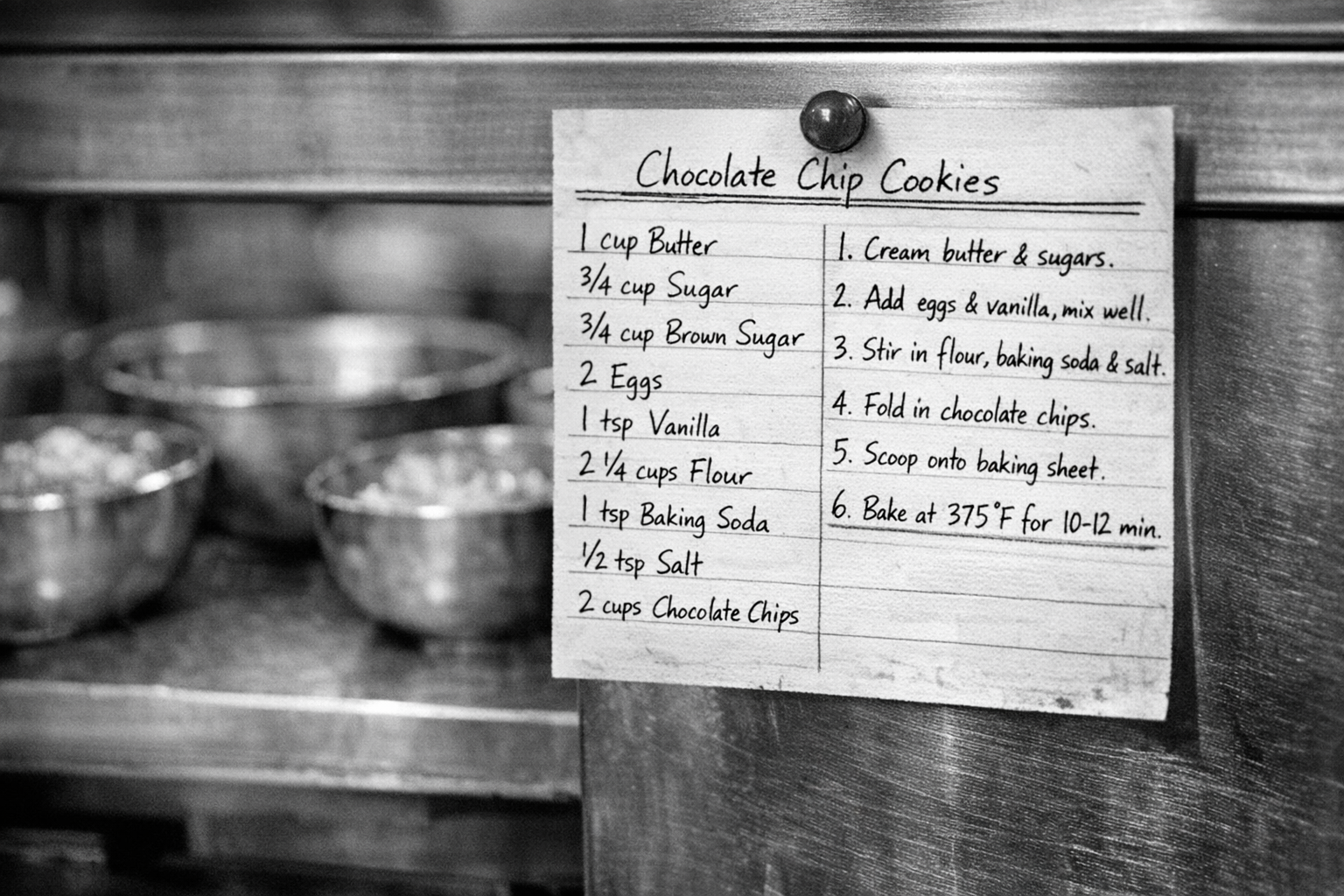 A handwritten recipe card pinned to a stainless steel kitchen station